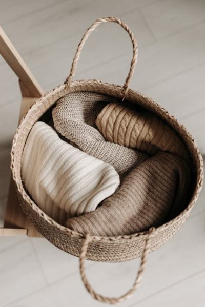 Top view of cozy sweaters in a woven basket on a wooden chair, perfect for autumn decor.
